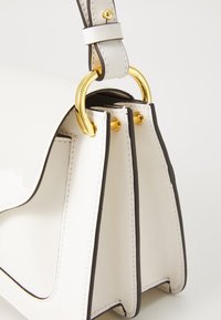 Witte leren handtas met zwarte accenten, met een gestructureerd ontwerp, gouden hardware en een dubbelgestikte handgreep.