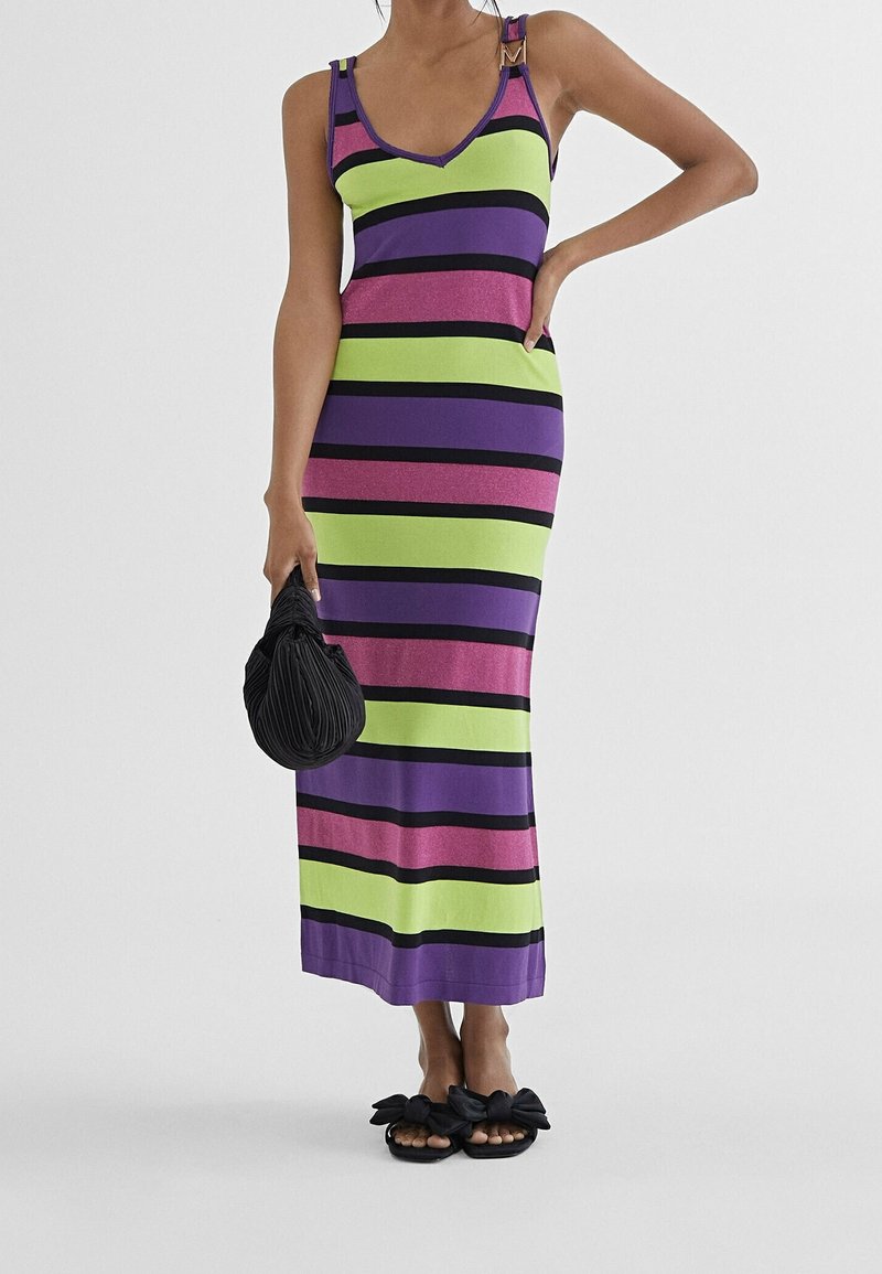 Randig klänning med gröna, lila och rosa horisontella ränder, med v-ringning och dekorerade axelremmar. Svart väska och sandaler.