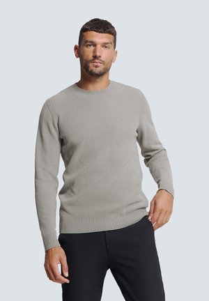 Grijze geribbelde trui met lange mouwen en een ronde hals, met een aansluitende zoom en een gladde textuur. Draagt met zwarte broek.