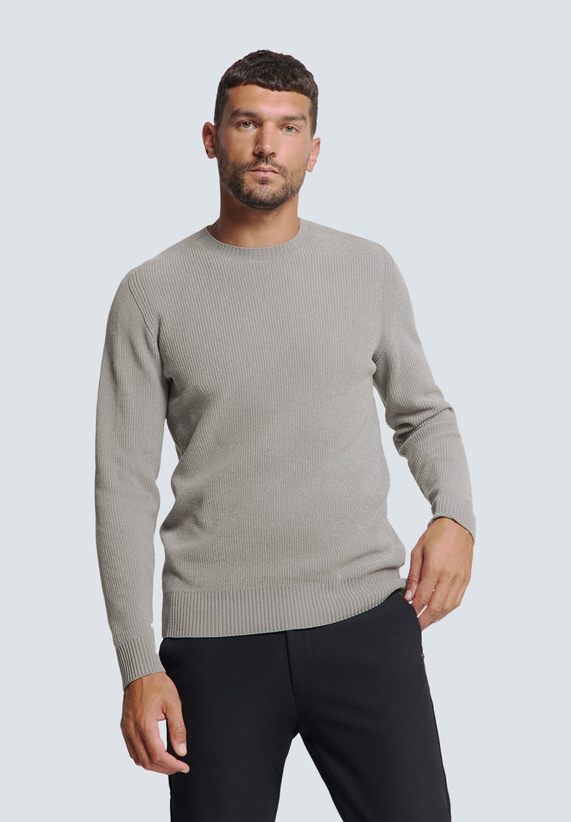 Grijze geribbelde trui met lange mouwen en een ronde hals, met een aansluitende zoom en een gladde textuur. Draagt met zwarte broek.