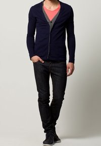 Cardigan blu navy su camicie sovrapposte grigie e rosa, abbinato a jeans scuri e scarpe blu. Tessuto testurizzato e design slim fit.