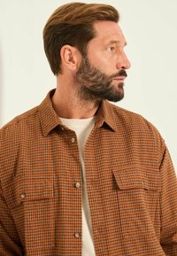 Braun karierte Hemd mit Knopfverschluss vorne, zwei Brusttaschen und einem lockeren Schnitt, aus einem strukturierten Stoff gefertigt.