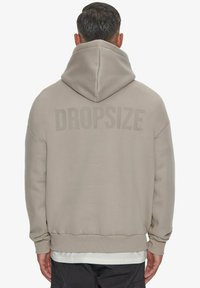 Hoodie beige avec une capuche à cordon, des poignets et un ourlet côtelés. Grande impression "DROPSIZE" au dos. Texture douce, design décontracté.