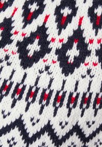 Motif de tissu tricoté avec des formes losanges blanches, bleu marine et petites rouges, disposées selon un dessin géométrique traditionnel.