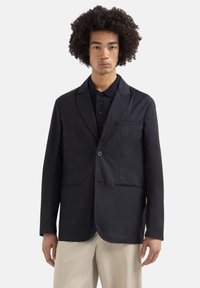 Blazer leggero nero con un solo pulsante, due tasche frontali, rever a estremità a punta e una texture liscia, abbinato a una polo scura.