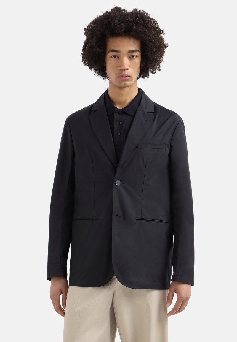 Blazer leggero nero con un solo pulsante, due tasche frontali, rever a estremità a punta e una texture liscia, abbinato a una polo scura.