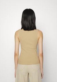 Top de alças bege com riscas, apresentando um design ajustado, com gola redonda e alças largas, combinado com calças bege claras.