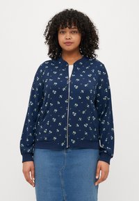 Veste aviateur navy avec motif floral en bleu clair et vert, fermeture zippée et bords côtelés aux poignets et à l'ourlet. Tissu doux avec une texture lisse.
