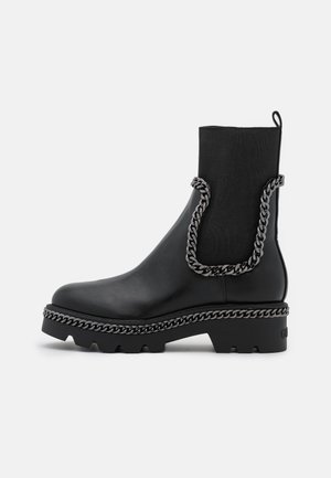Bottine en cuir noir avec une tige en tissu extensible et des détails décoratifs en chaîne argentée. Semelle épaisse et robuste avec une finition texturée.