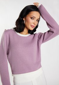 Lila cropped trui met een witte ribbelkraag en -manchetten. Kenmerkt zich door gouden hardware accenten op de schouder. Zacht en gestructureerde stof.