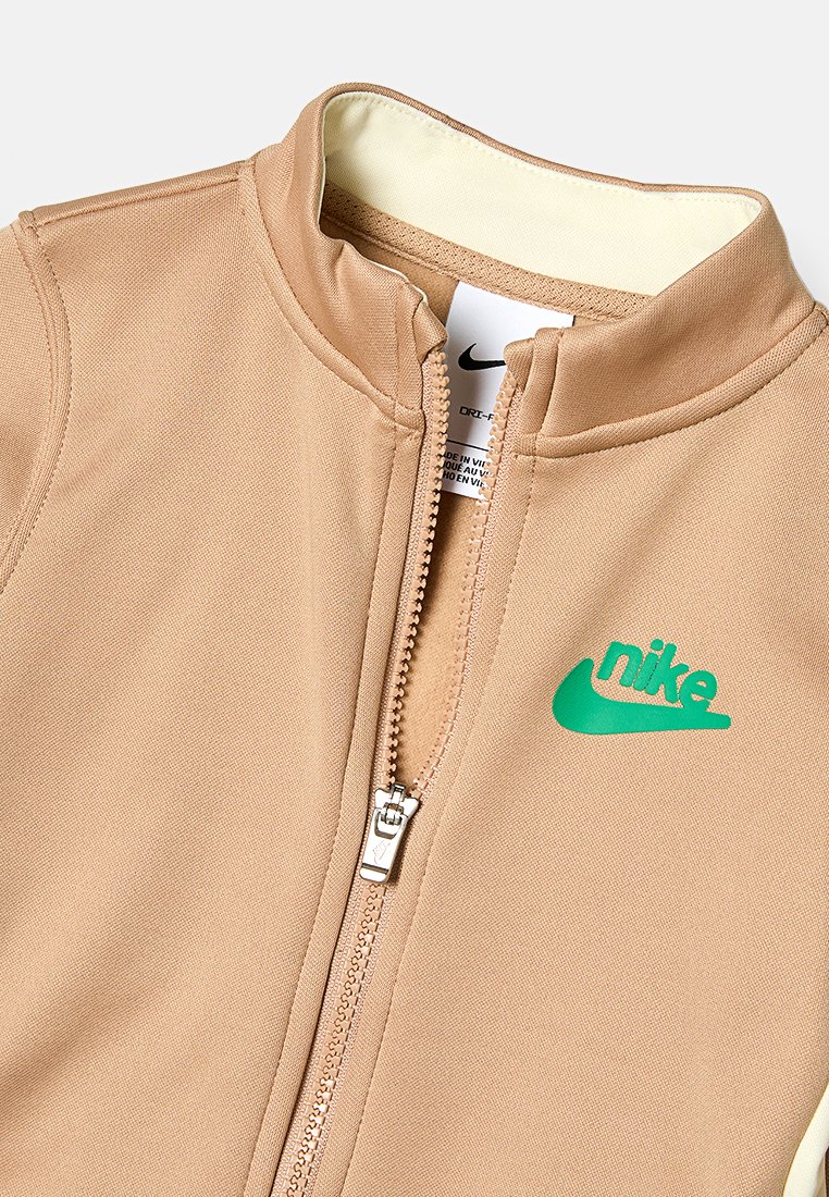 Beżowa kurtka zapinana na zamek, wykonana z gładkiego materiału. Posiada jasny wewnętrzny kołnierz oraz zielone logo Nike z przodu.
