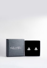 Silvertriangulära stiftörhängen presenterade i en svart sammetslåda. Lådan har en strukturerad mörkgrå utsida med vit logotyp.