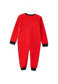 Pyjama en polaire rouge avec manches longues, poignets noirs et fermeture éclair dans le dos. Présente un design de panneaux latéraux à motifs. Texture douce et forme épurée.