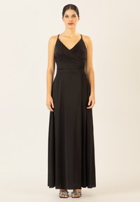 Schwarzes Maxikleid mit V-Ausschnitt und Wickeldesign, aus glattem Stoff gefertigt. Verfügt über dünne Träger und einen fließenden Rock, kombiniert mit verzierten Sandalen.