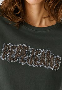 Tmavě zelené bavlněné tričko s nápisem "PEPE JEANS" v velkých, třpytivých kamínkách na přední straně. Kulatý výstřih a krátké rukávy.