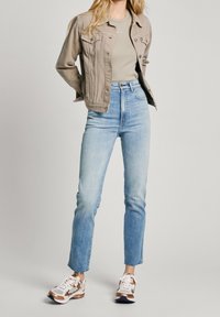 Ljusbeige denimjacka, ljusgrå topp och ljus tvättade högmidjade jeans med fransade fållar. Skorna har en blandning av vitt, beige och marinblå färger.