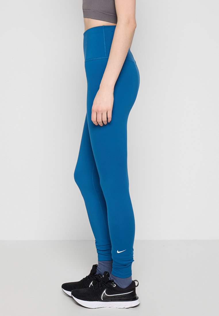 Blaue hochgeschnittene Leggings aus dehnbarem Stoff, mit einer glatten Textur und einem kleinen weißen Logo am linken Knöchel.