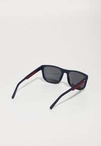 Navy blue sunglasses with square lenses, grey tinted lenses, and red accents on the arms. Made from a matte material with a smooth texture.