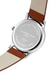 Fond de montre en acier inoxydable rond avec des détails gravés ; bracelet en cuir brun avec un dessous crème ; design minimaliste, lettres claires.