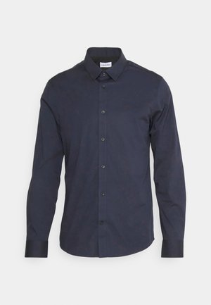 Navy button-up shirt made of smooth fabric, featuring a pointed collar, long sleeves, black buttons, and a subtle logo on the chest.