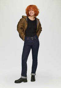 Donkerdenim jeans met een slim fit, met opgerolde mouwen en contrasterende stiksels. Gecombineerd met een zwarte top en een olijfgroene pufferjack.