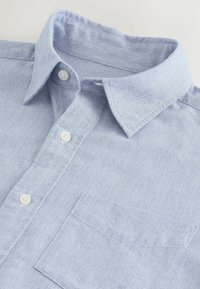 Hellblaues Button-Down-Hemd aus strukturiertem Stoff. Verfügt über einen klassischen Kragen, zwei vordere Knöpfe und eine Brusttasche.