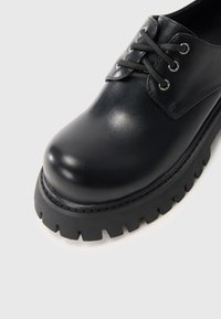 Scarpa stringata in pelle nera con punta arrotondata e suola in gomma spessa e texture, dotata di suola profonda per trazione e durata.