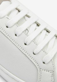 Baskets en cuir blanc avec tige texturée, lacets plats blancs et coutures contrastées. Présentent une pointe arrondie et une languette rembourrée.
