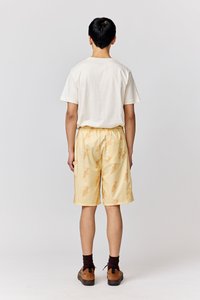 Yellow shorts with fish pattern, elastic waistband, and a back pocket. Paired with a white t-shirt and brown shoes with dark socks.