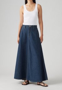 Džínová maxi sukně s vysokým pasem, A-liniovým střihem a viditelným švem. V kombinaci s bílým tílkem a černými žabkami.