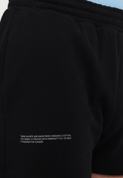 Schwarze Shorts aus Bio-Baumwolle mit strukturiertem Finish und elastischem Bund. Weißer Text auf dem Stoff beschreibt die Frischebehandlung mit pprmint™ Öl.