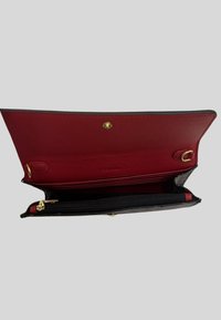 Portafoglio nero con interno rosso, dotato di superficie texturizzata, scomparto con zip e accentuazioni in oro. Si apre con una chiusura a scatto.