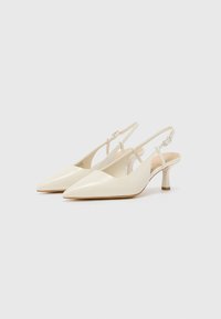 Kremfargede slingback hæler med spiss tå, glatt lærtekstur, lav stilettotipo og justerbar stropp.