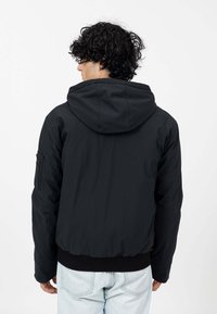 Zwarte hoodie-jack van gladde stof, met een geribbelde zoom. Het ontwerp bevat een zijzak en heeft een relaxte pasvorm, getoond vanuit de achterkant.
