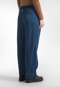 Wijde denim broek met een elastische tailleband, diepblauwe kleur en een gladde textuur. Draagt een relaxed fit met zwarte sneakers.