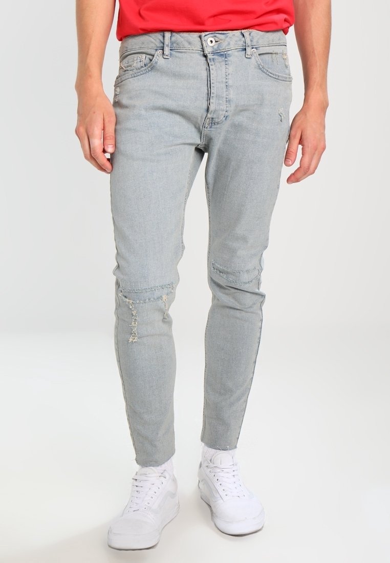 Jeans ajustados de denim azul claro con detalles desgastados, cinco bolsillos y una cinturilla estándar. Llevados con zapatillas blancas.