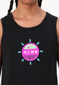 Črna majica na naramnice z okroglo grafiko, ki prikazuje besedo "nike" v beli barvi, obdano s sunburst obliko v roza in zeleni barvi.