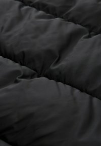 La tela acolchada negra presenta una textura suave con secciones acolchadas. El material es ligero y tiene un acabado mate.