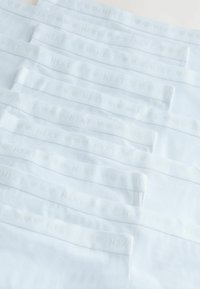 Weiße Baumwollunterwäsche, ordentlich gestapelt, mit einem weichen Bund, der mit "NEXT" und Herzmustern geprägt ist, und einer glatten, matten Textur.
