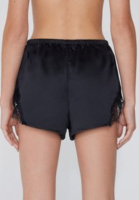 Zwarte satijnen shorts met een gladde textuur, voorzien van kantdetails aan de zijkanten en een elastische tailleband voor extra comfort.