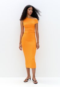 Robe midi orange ajustée en tissu extensible. Design une épaule avec un détail froncé à la taille. Le modèle porte des sandales à lanières noires.