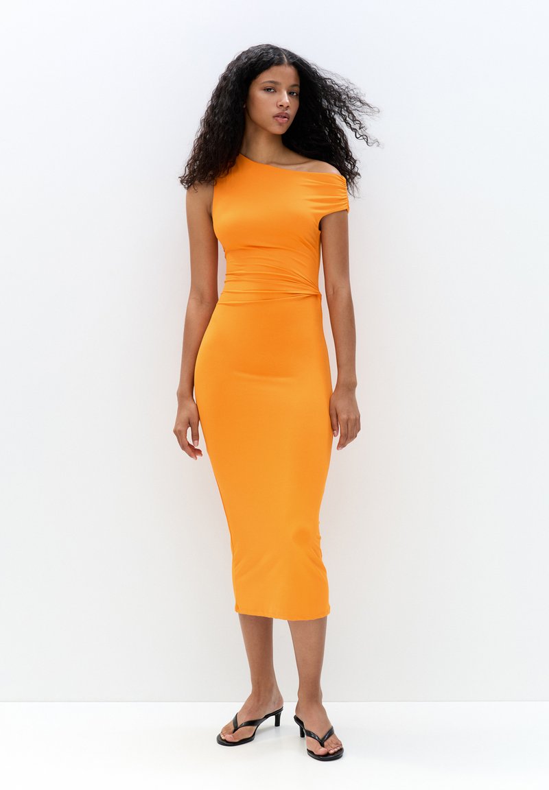 Robe midi orange ajustée en tissu extensible. Design une épaule avec un détail froncé à la taille. Le modèle porte des sandales à lanières noires.