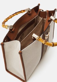 Sac en toile beige avec des accents marron et une poignée en bambou. Comprend des compartiments zippés et un design texturé et structuré. Détails en matériel doré.