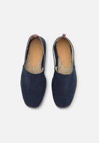 Námornícke plátenné espadrilky s jutovou podrážkou, s béžovou vnútornou podšívkou a červenobielo-modrým prúžkovaným detailom na päte.