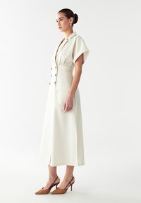 Vahajasest linast kleit lühikeste varrukatega, nööpidega ees ja kahe küljetaskuga; sobitatud pruunide mustriliste ülemiste kontsadega.