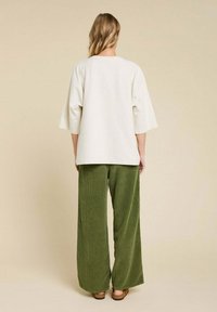 Haut en crème, ample avec de larges manches, associé à un pantalon en velours côtelé vert à jambe large. Texture lisse et silhouette décontractée.
