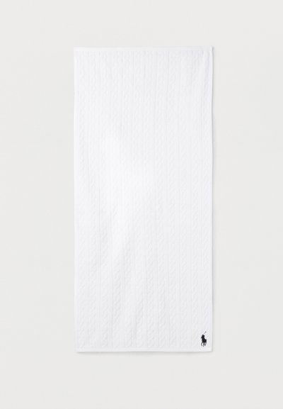 Λευκή ορθογώνια πετσέτα με κατακόρυφη υφή πλεκτού κάμπιου και μικρό μαύρο λογότυπο παίκτη πόλο με άλογο στην κάτω δεξιά γωνία.