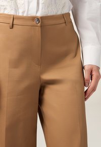 Beige Hosen aus glattem Stoff, mit einer Fronttasche, einem Knopfverschluss und geraden Beinen. Das Material wirkt leicht und weich.