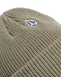 Beige gebreide wolmuts met een klein zwart-wit geometrisch logo-patch op de geribbelde rand.