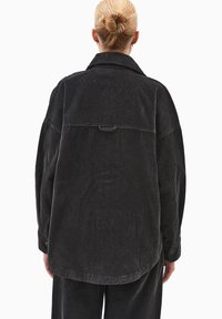 Sort fløjl jakke med en afslappet pasform, der har en rygskuldre, sidelommer og knapmanchetter. Strukturert vertikal ribbning er synlig.